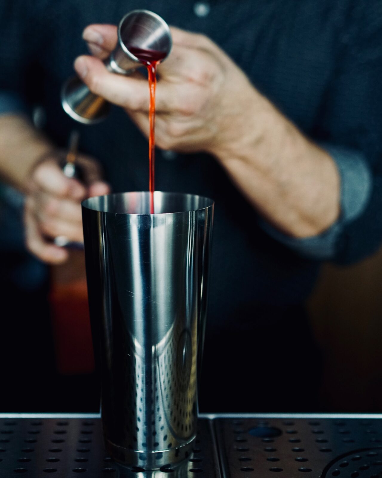 A bartender building a cocktail in a mixing tin