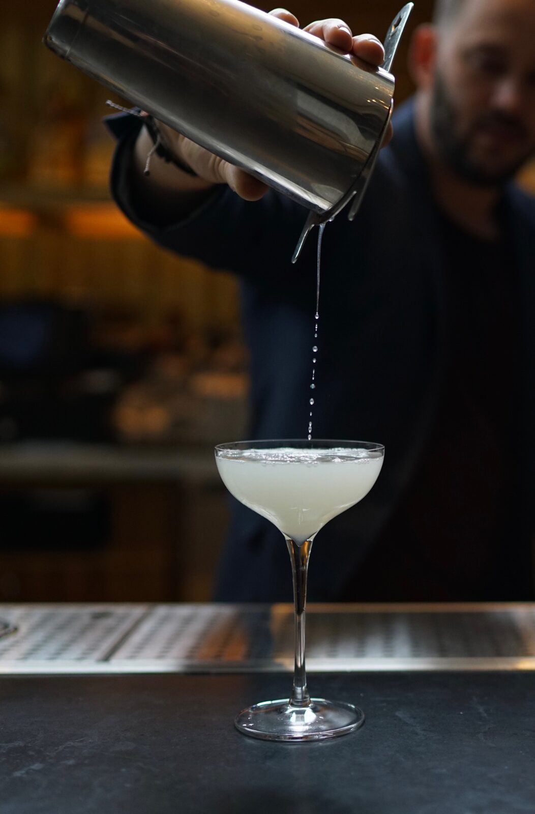 A bartender pouring a pale cocktail into a coupe