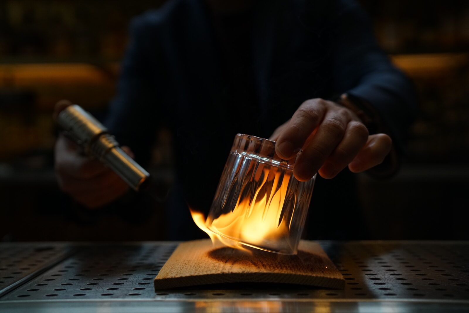 A bartender flaming an aromatic cocktail over the bar